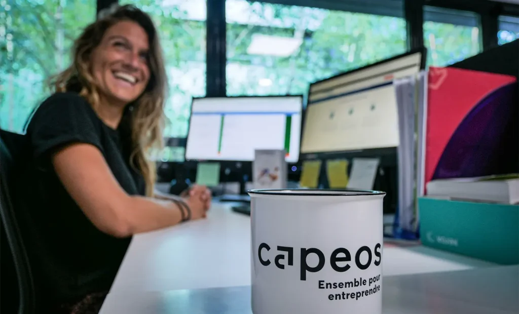 Collaboratrice Capeos souriante à son bureau, mug Capeos « Ensemble pour entreprendre » au premier plan