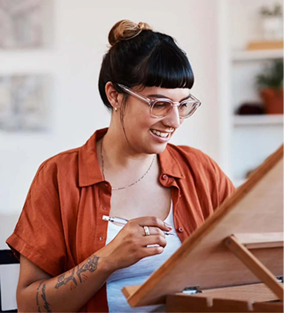 Illustratrice souriante dessinant sur sa table à dessin inclinée dans son atelier