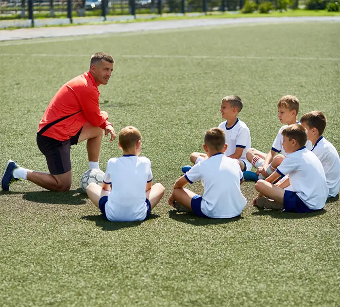 Entraîneur de football donnant des consignes à de jeunes joueurs assis sur un terrain
