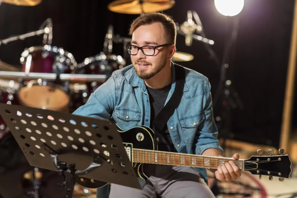 Musicien guitariste jouant de la guitare électrique devant un pupitre, batterie en arrière-plan dans un studio