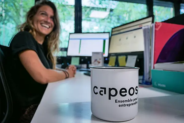 Collaboratrice Capeos souriante à son poste, mug Capeos au premier plan